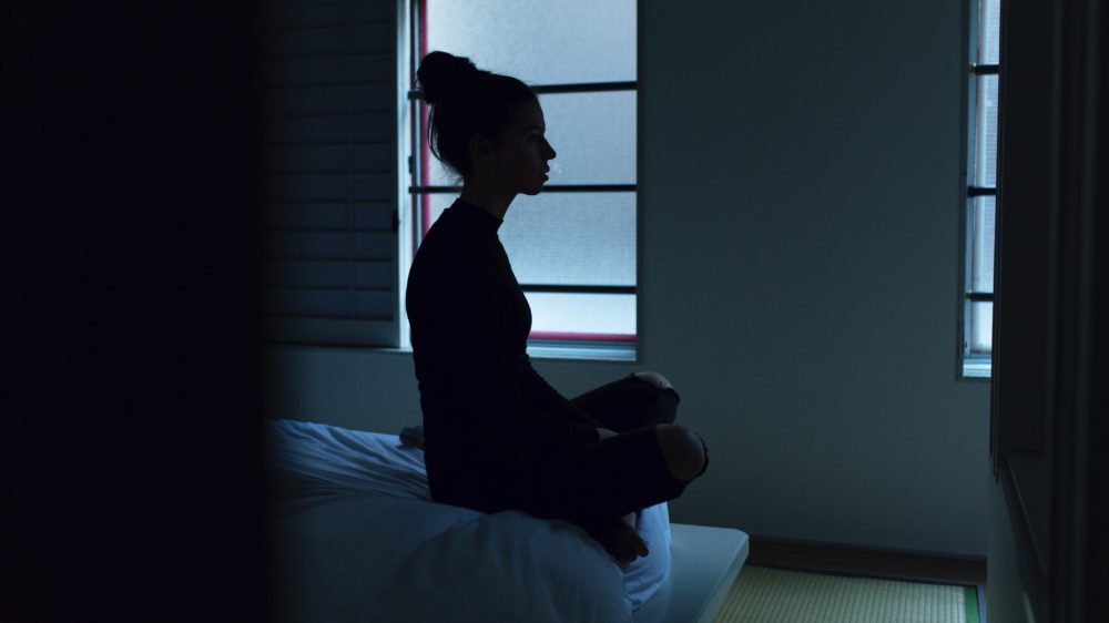 Incarcerated teen girl sits on bunk practising mindfulness.