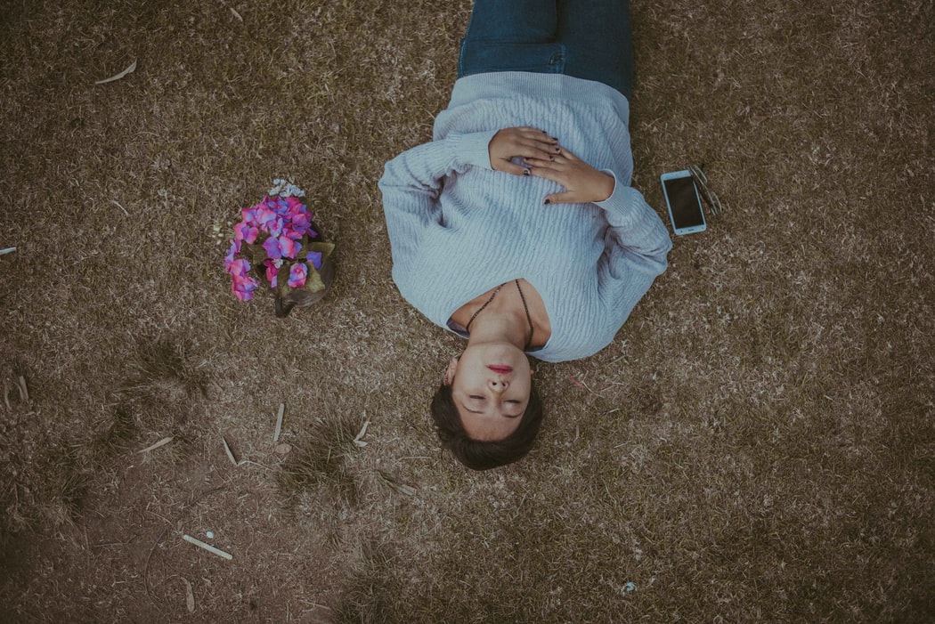 A person laying on grass taking time to feel sensations in their body.