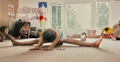 Yoga Teacher in wide legged forward fold in a sunny studio surrounded by students