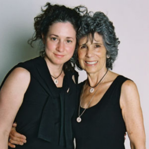 A woman in her 20s stands arm in arm with a woman in her 40s