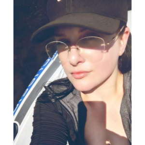 Photo of woman with glasses, in bright sunlight, eyes shadowed by a baseball cap. Sitting in a boat. 