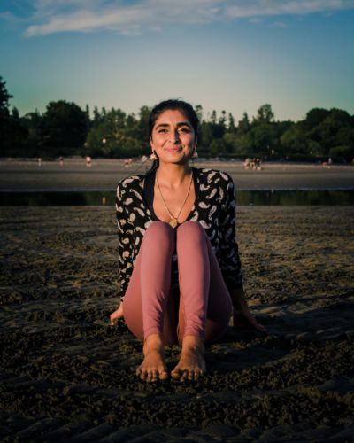 A South Asian woman sits on a sandy beach smiling