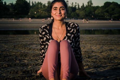 A South Asian woman sits on a sandy beach smiling