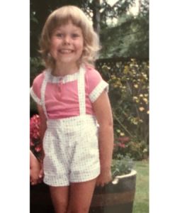 A little girl about 5 years old with blond hair grins into the camera, a photograph of Melissa Holt as a child. 